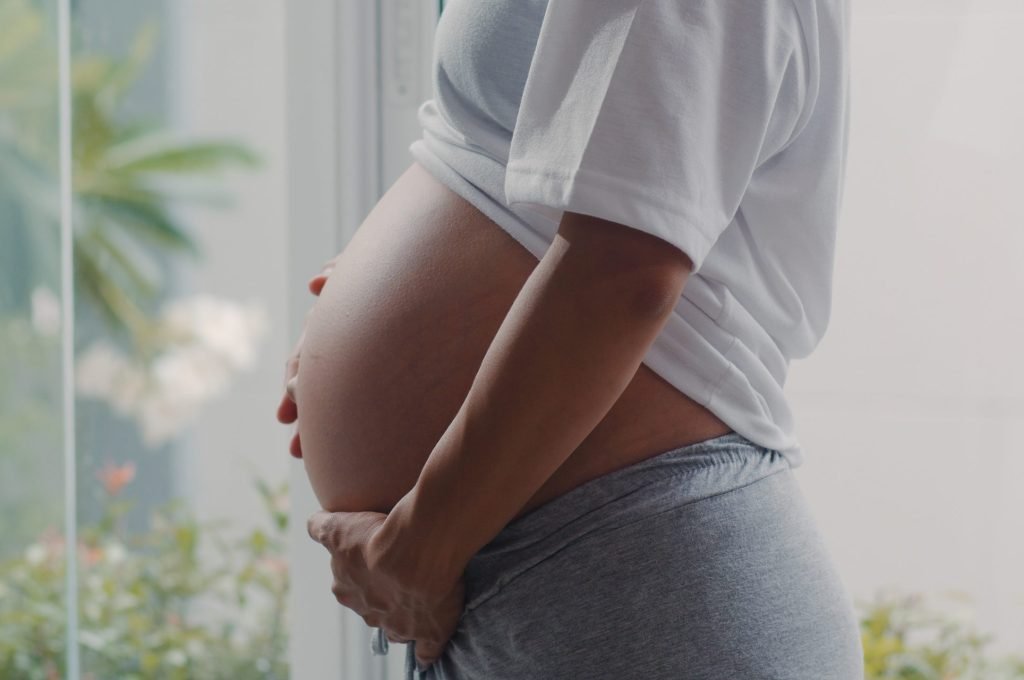Young Asian Pregnant woman holding her belly talking with her child. Mom feeling happy smiling positive and peaceful while take care baby, pregnancy near window in living room at home concept.